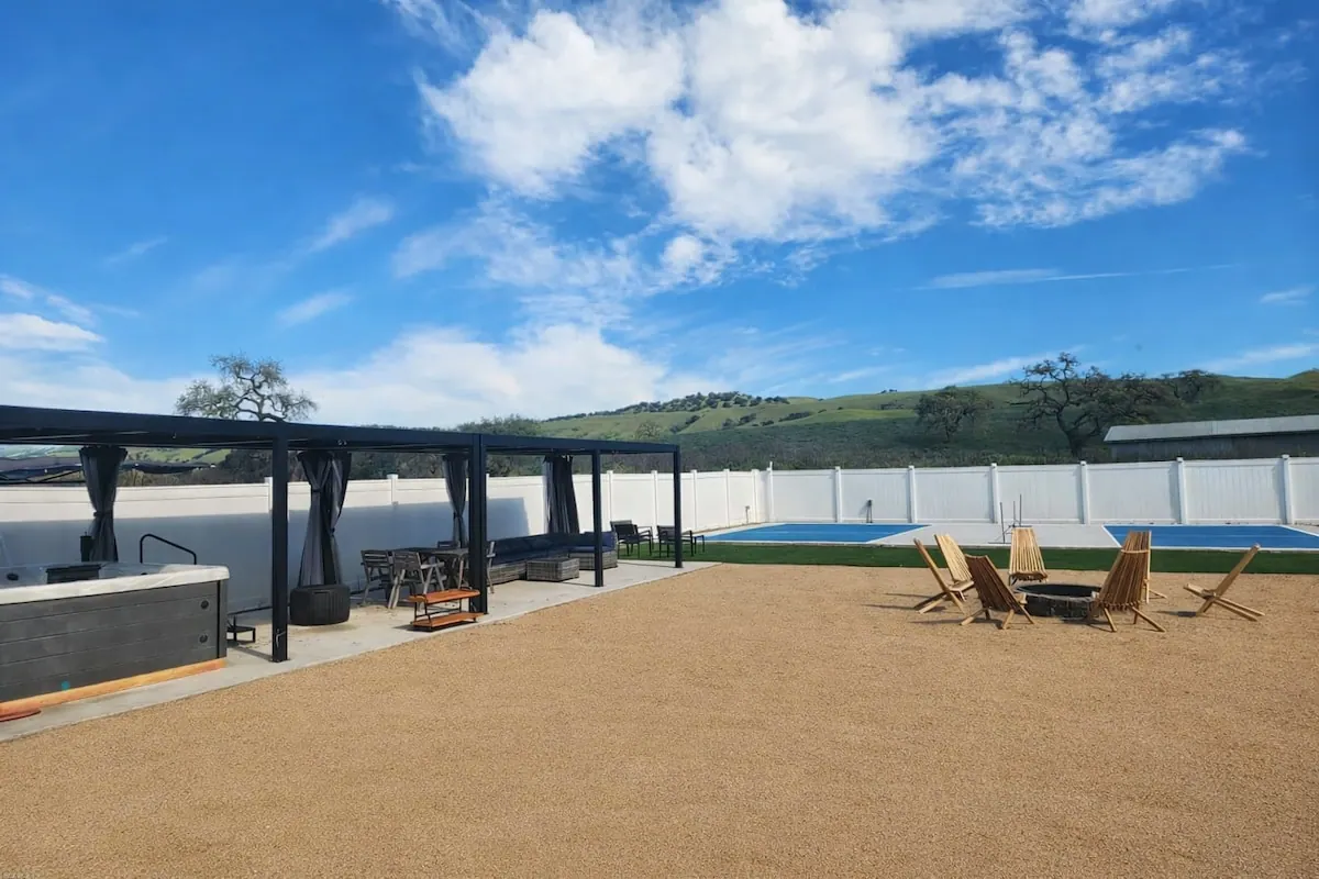 Backyard patio with the heated hot tub under a pergola, sport court and hills beyond