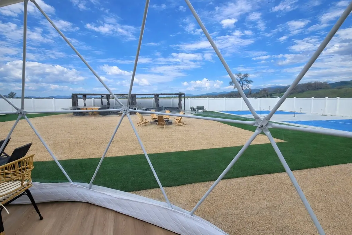View from inside a dome toward the fire pit, lawn and blue sport court