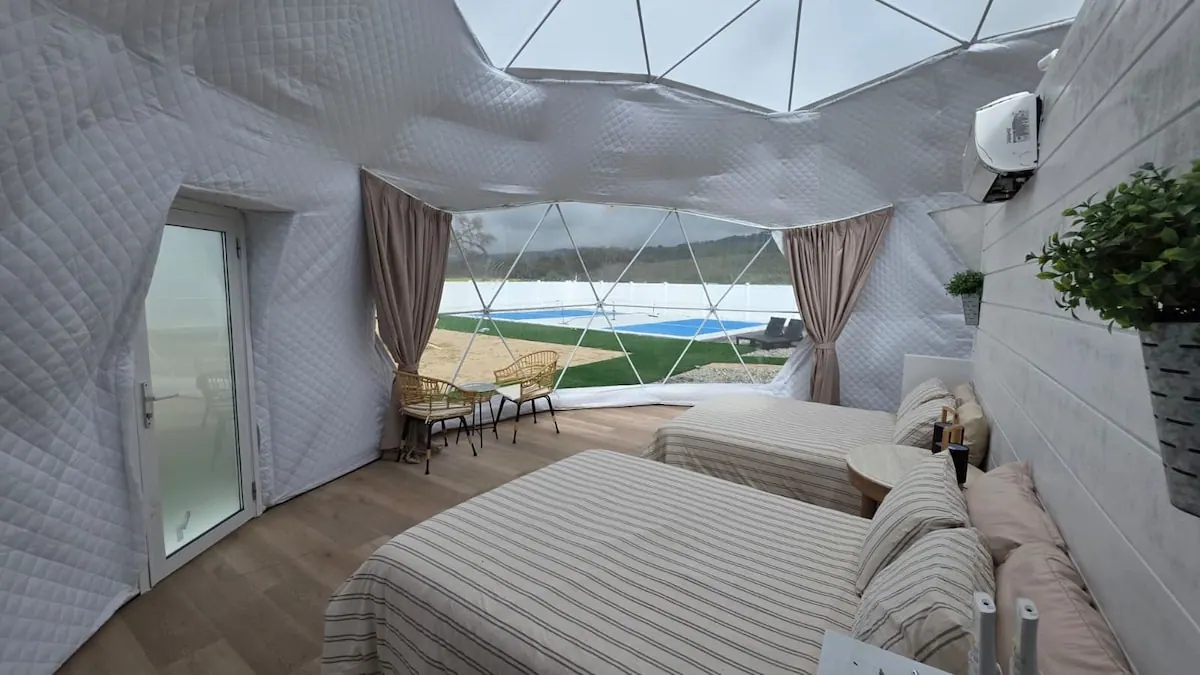 Dome interior with striped beds and rattan chairs looking out to the sport court